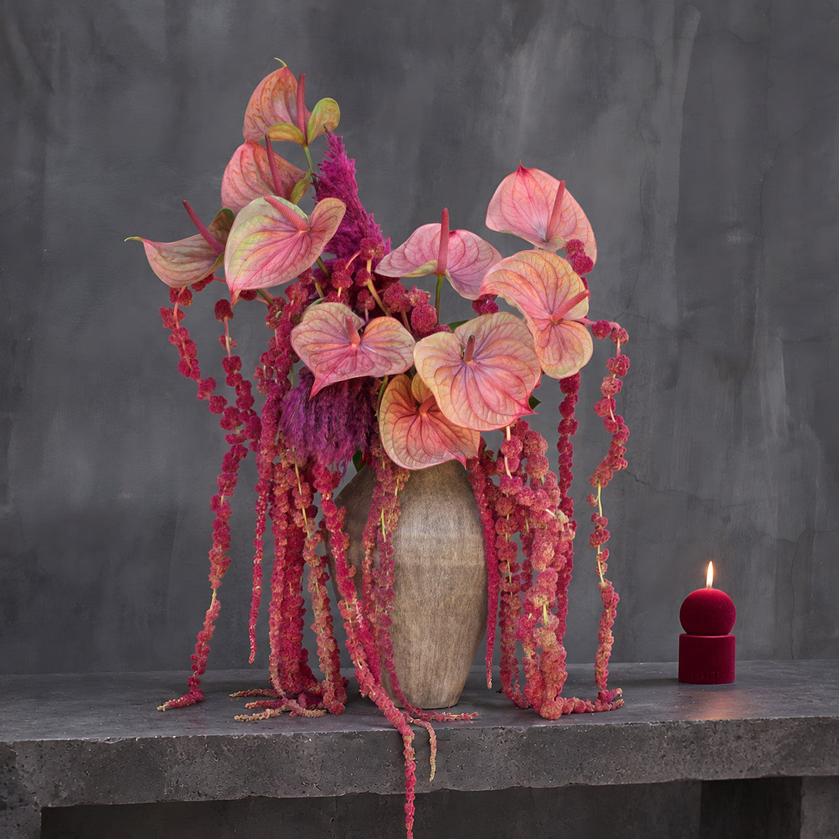 Medusa arrangement of coral-pink anthuriums, magenta plumes and hanging red amaranthus in a ribbed taupe ceramic vase