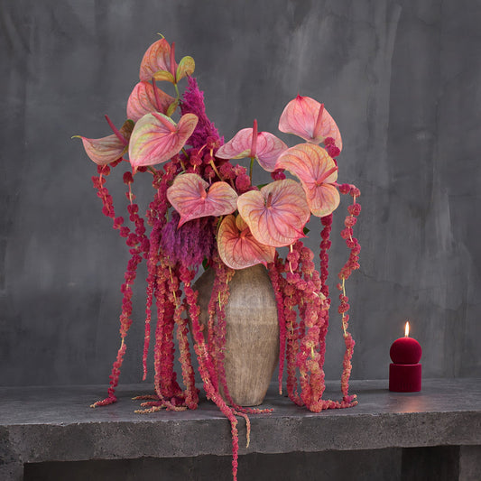 Medusa arrangement of coral-pink anthuriums, magenta plumes and hanging red amaranthus in a ribbed taupe ceramic vase